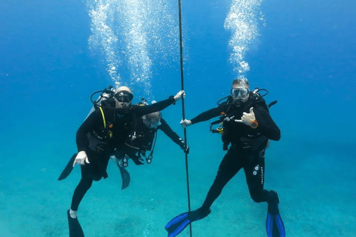 Three divers underwater holding a rope and making hand gestures with blue flippers visible.